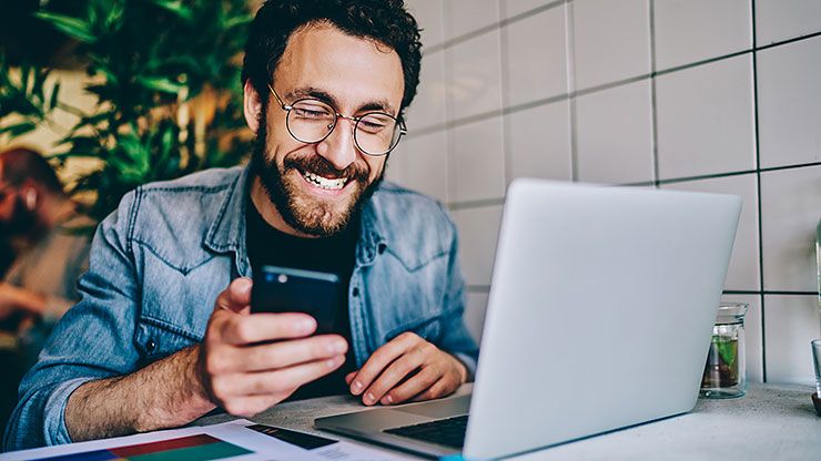 Mann mit Laptop und Smartphone, zeigt CARAT Planner-App mit Logo 'CARAT PLANNER' und Text 'Frequenzbringer für Ihre Website
